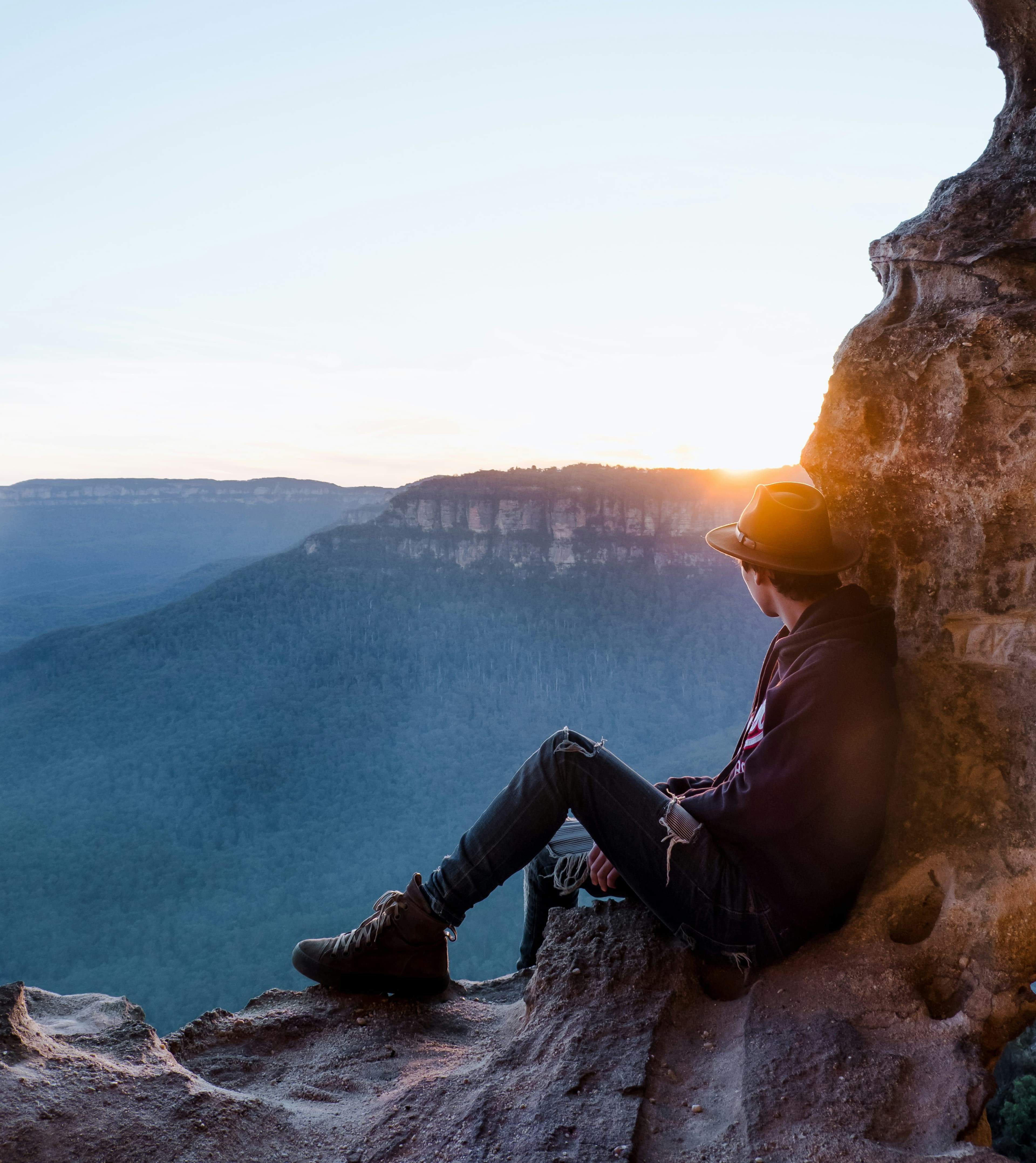 Leio Mclaren sitting on a cliffside, looking out to the sunrise