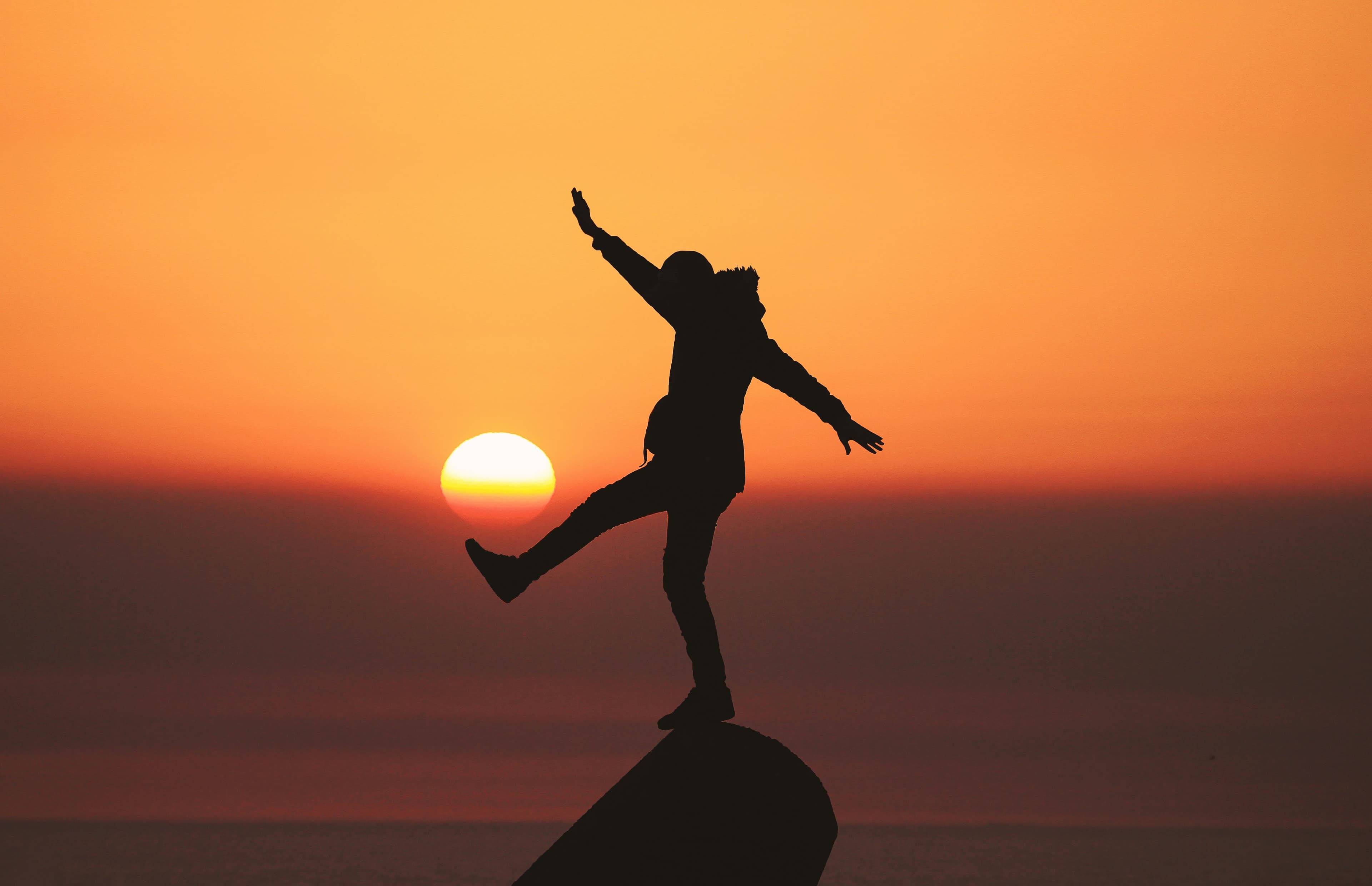 a silhouette of a person stepping off of a mountain peak